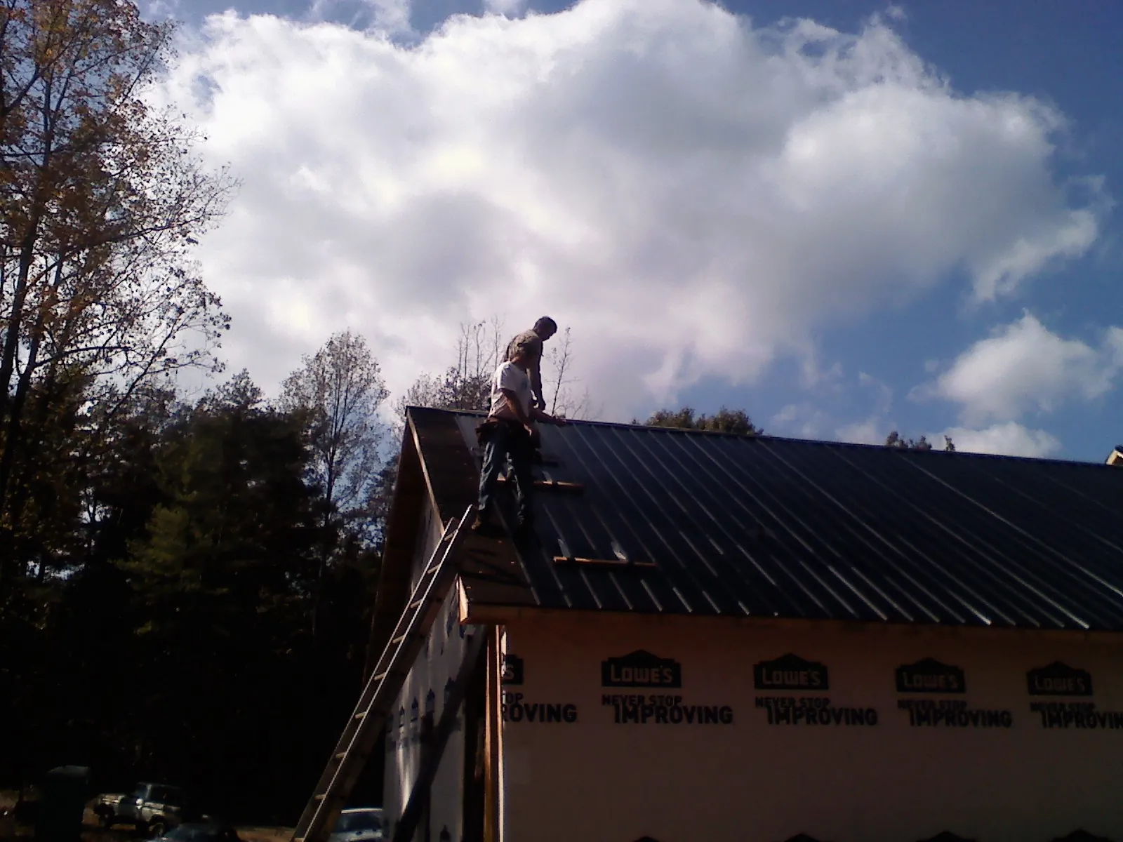Roofer fastening dark metal panels high against a cloudy sky, from a Roof Inspection job in Sandy